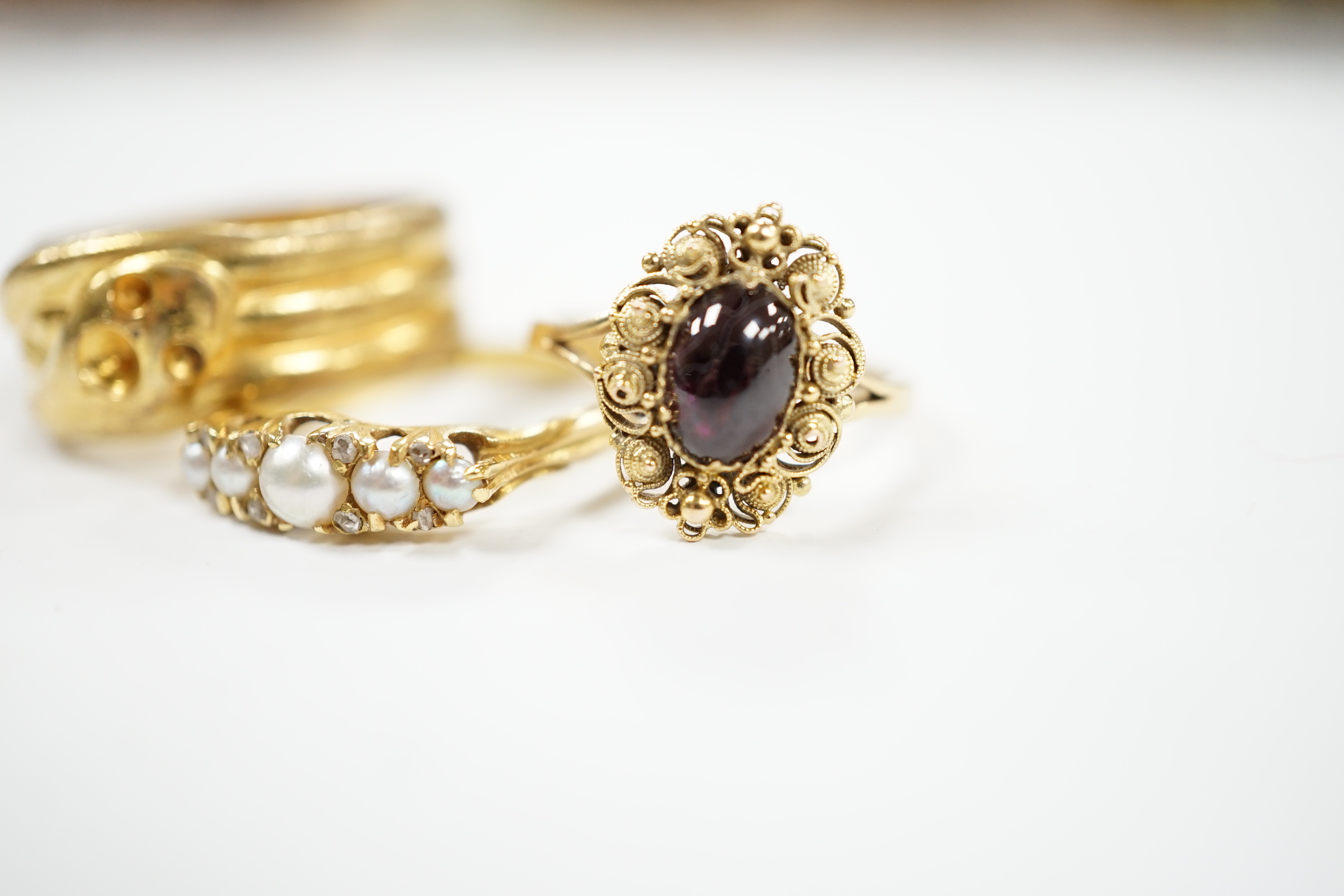 A yellow metal and cabochon garnet set ring, an Edwardian 18ct and graduated split pearl set half hoop ring, with diamond chip spacers and one other ring.